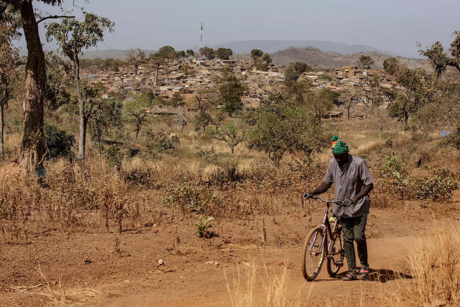 A man walks with his bike with a view of a town built near a gold mining site in the Kedougou region of Senegal on Thursday, Jan. 16, 2025. (AP Photo/Annika Hammerschlag)
