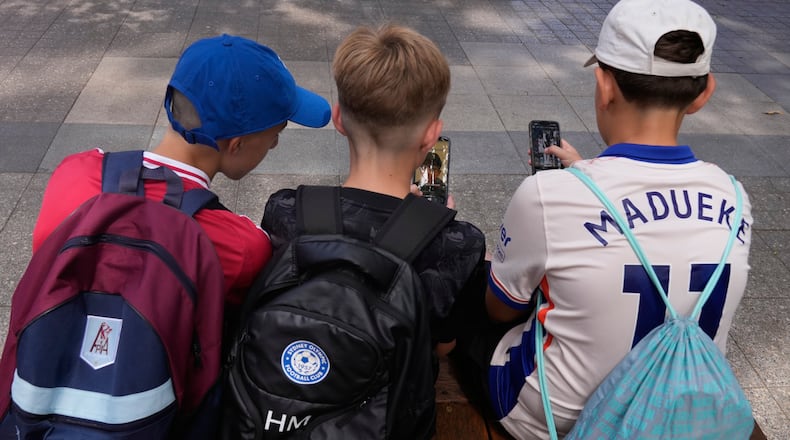 Hugo Winwood-Smith, right, Hardy Macpherson and Edan Abou, left, all 11-years-old, use their phones while sitting outside a school in Sydney, Monday, Dec. 8, 2025. (AP Photo/Rick Rycroft)