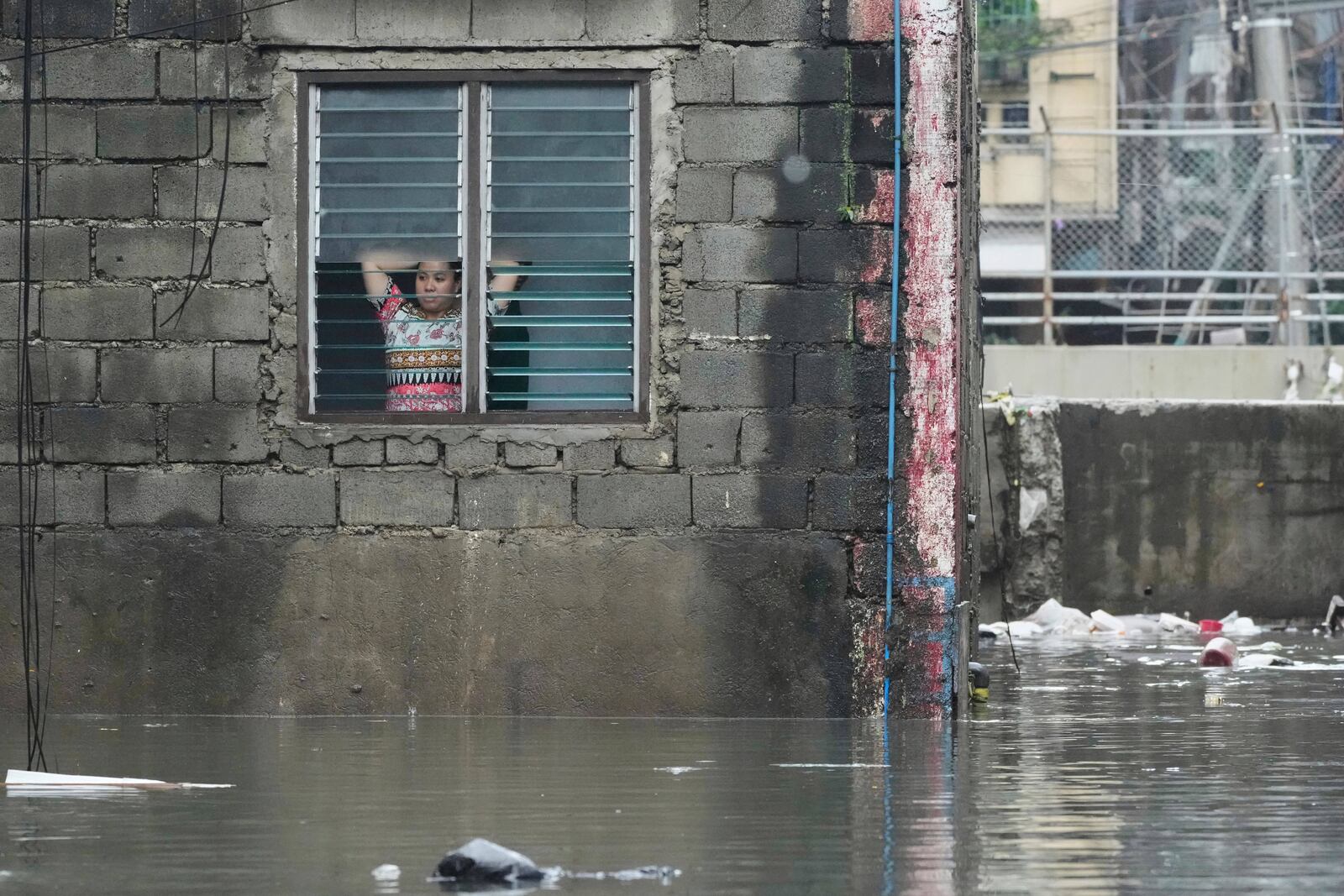 A woman looks outside from her flooded home following tropical storm Wipha fueled monsoon rains in Quezon city, Philippines on Tuesday, July 22, 2025. (AP Photo/Aaron Favila)