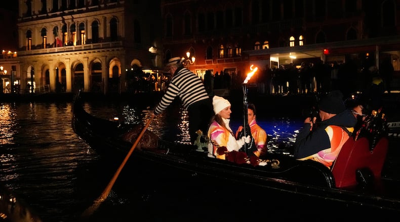 A torchbearer holds an Olympic torch flame on the Grand Canal in Venice, Italy, Thursday, Jan. 22, 2026, and its journey will conclude in Milan on February 6 for the Winter Olympics opening ceremony. (AP Photo/Luca Bruno)