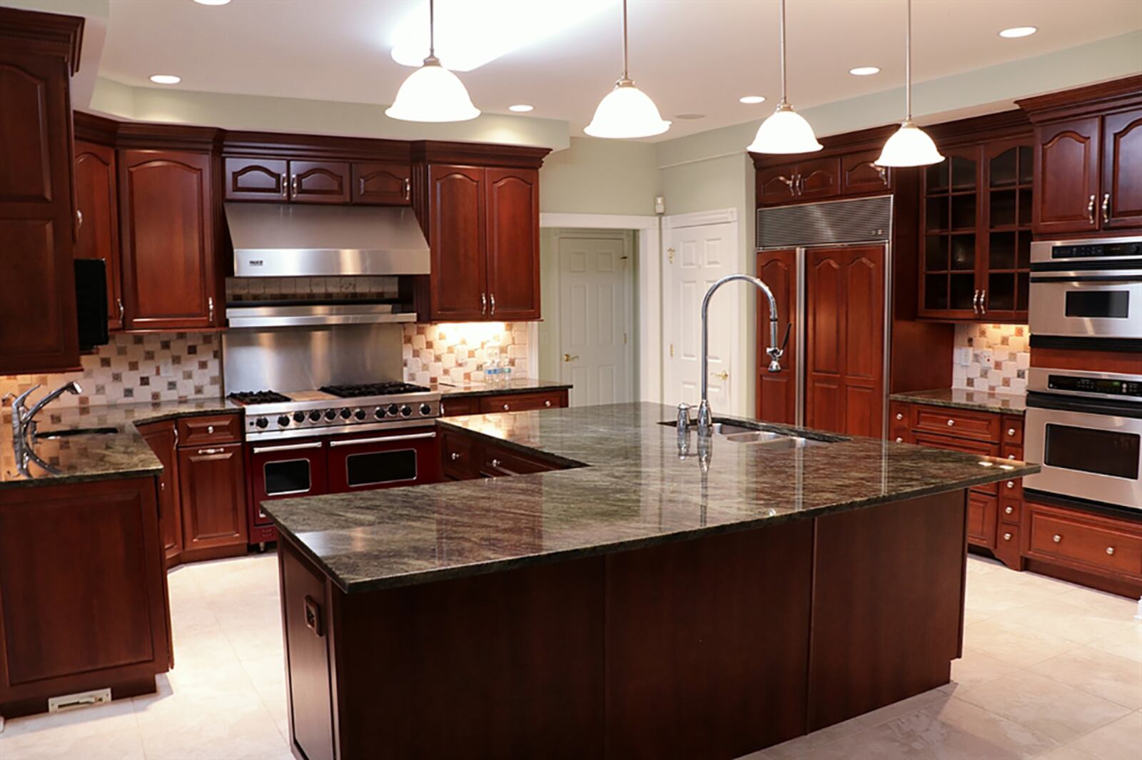 The kitchen has an abundance of cherry cabinetry and granite countertops. An L-shaped island has a triple sink with nearby dishwasher and extends into a breakfast bar seating area with hanging light fixtures above. CONTRIBUTED PHOTO BY KATHY TYLER