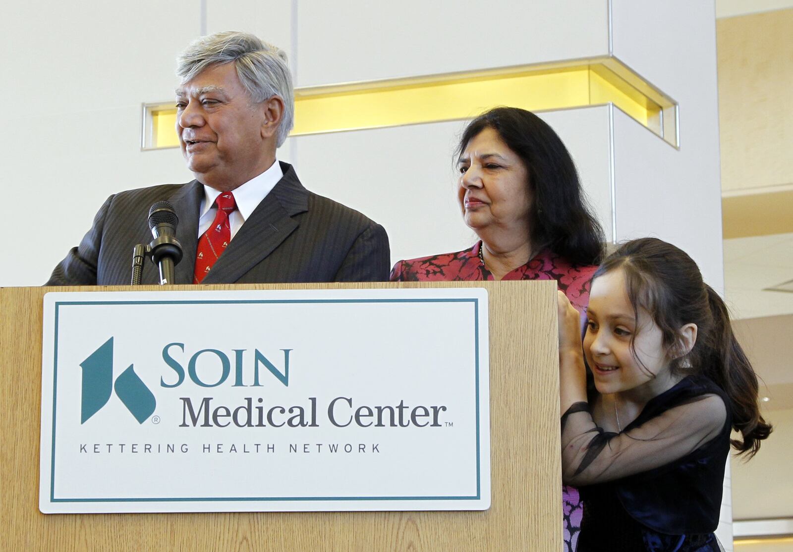 Raj and Indu Soin's granddaughter Mira, then 8, peeks around the lectern as Raj Soin speaks at a ribbon-cutting for Soin Medical Center in Beavercreek in this February 2012 file photo. 