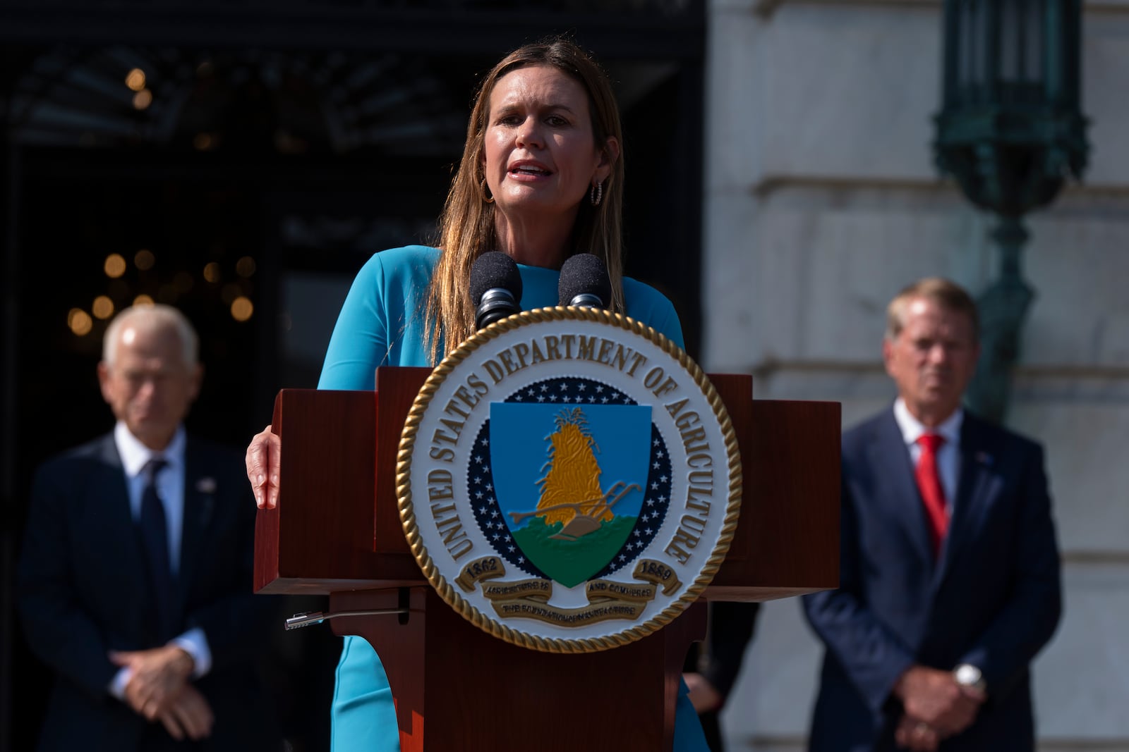 Arkansas Gov. Sarah Huckabee Sanders, center, with White House trade counselor Peter Navarro, left, and Nebraska Gov. Jim Pillen, right, speaks during a news conference at the Department of Agriculture to rollout the USDA'S National Farm Security Action Plan and discuss actions being taken to protect American agriculture from foreign threats in Washington, Tuesday, July 8, 2025. (AP Photo/Manuel Balce Ceneta)