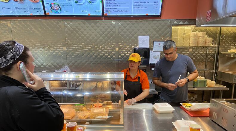 Syeda Gardevi, left, and Muhamad Najam, both employees of Deg’s Flame Grilled Chicken, serve one of their few customers of the day Tuesday evening. Gardevi, assistant manager, and Najam, the general manager, are the two remaining employees of the restaurant, located in the Mall at Fairfield Commons. Owner Naveed Haq said he was recently forced to lay off seven part-time and hourly employees after sales declined as people stopped going to the mall to avoid spreading or contracting the coronavirus. ISMAIL TURAY JR./Staff