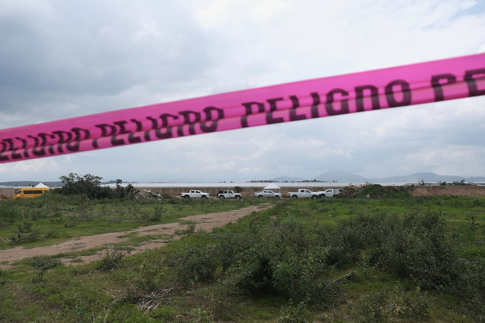 Danger warning tape streches along a Nextipac ranch where prosecutors say bodies were discovered in a mass grave during excavations for the construction, in the Zapopan municipality, Jalisco state, Mexico, Friday, July 11, 2025. (AP Photo/Alejandra Leyva)