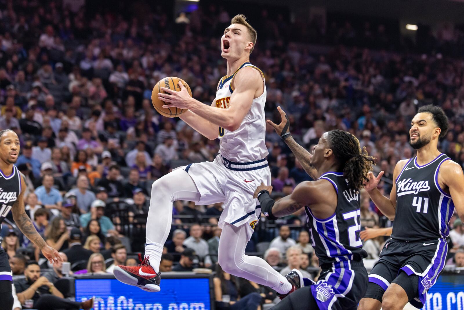 Denver Nuggets guard Christian Braun, center, makes a layup past Sacramento Kings guard Keon Ellis (23) during the first half of an NBA basketball game Wednesday, April 9, 2025, in Sacramento, Calif. (AP Photo/Sara Nevis)