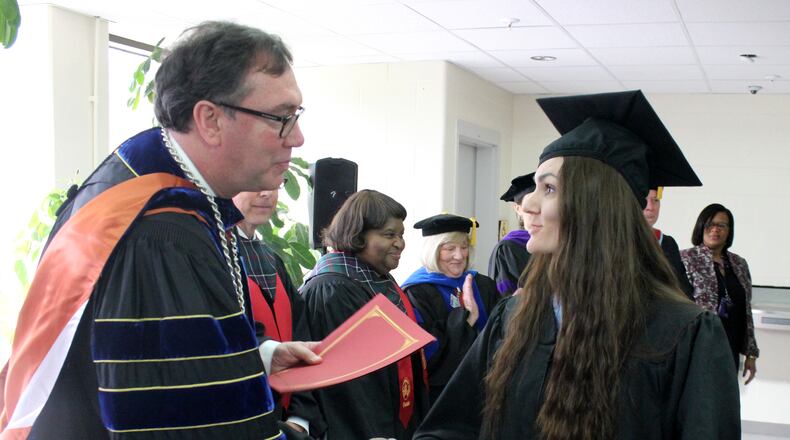 Jamie Belville shakes Sinclair President Steven Johnson’s hand as she receives her certificate during Monday’s ceremony at Dayton Correctional Institute. CHUCK HAMLIN/STAFF