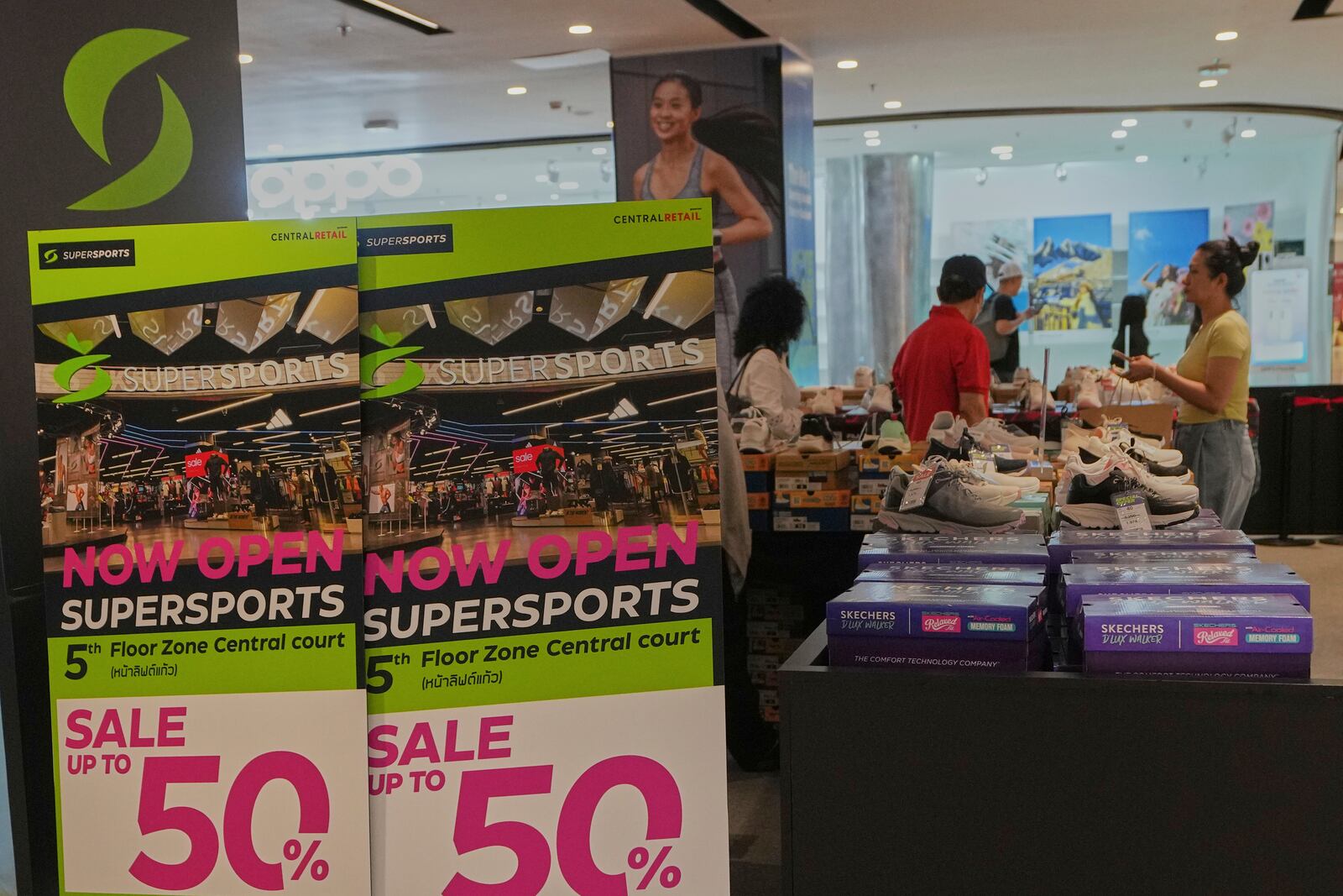Shoppers are seen behind a sales advertisement at a shopping mall in Bangkok, Thailand, Wednesday, April 9, 2025. (AP Photo/Sakchai Lalit)