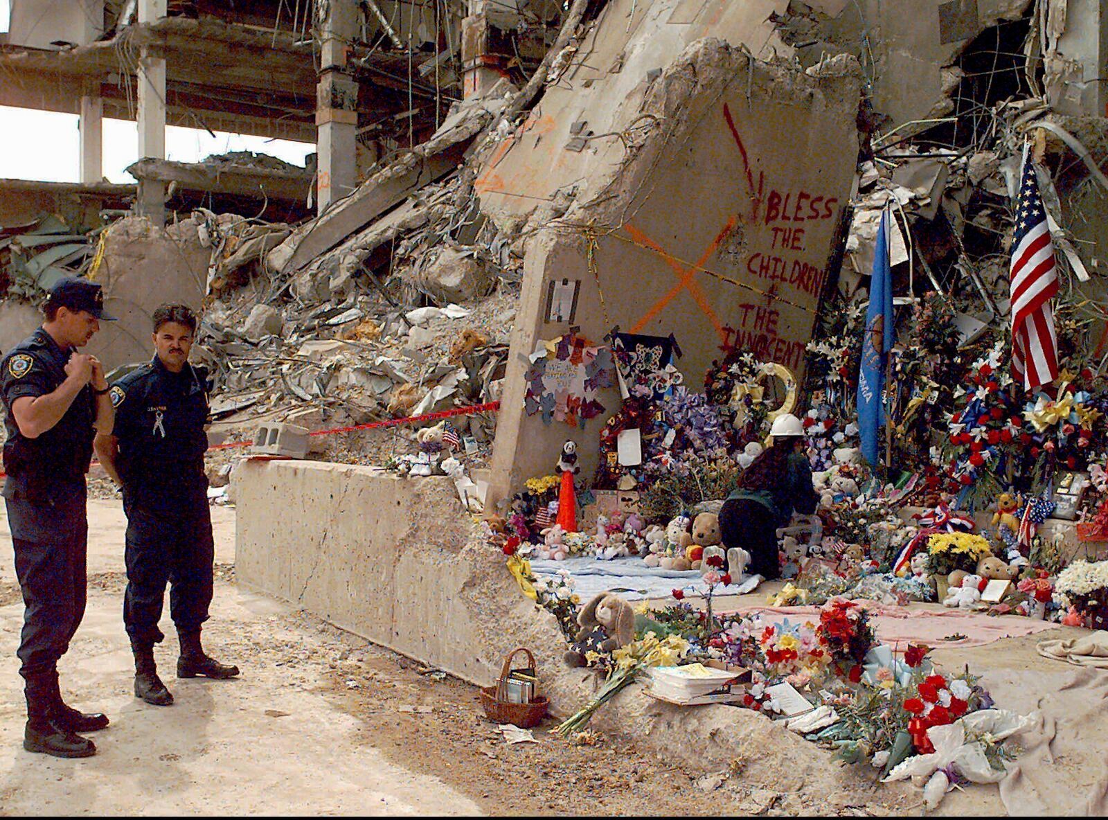 FILE - Officials stand near the Alfred P. Murrah Federal Building as workers place flowers and memorial items at the scene of the explosion in Oklahoma City on May 5, 1995. (AP Photo/J. Pat Carter, File)