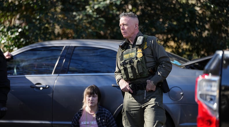 U.S. Border Patrol Commander at large Gregory Bovino, right, looks on as a detainee sits by a car, Monday, Nov. 17, 2025, in Charlotte, N.C. (AP Photo/Matt Kelley)