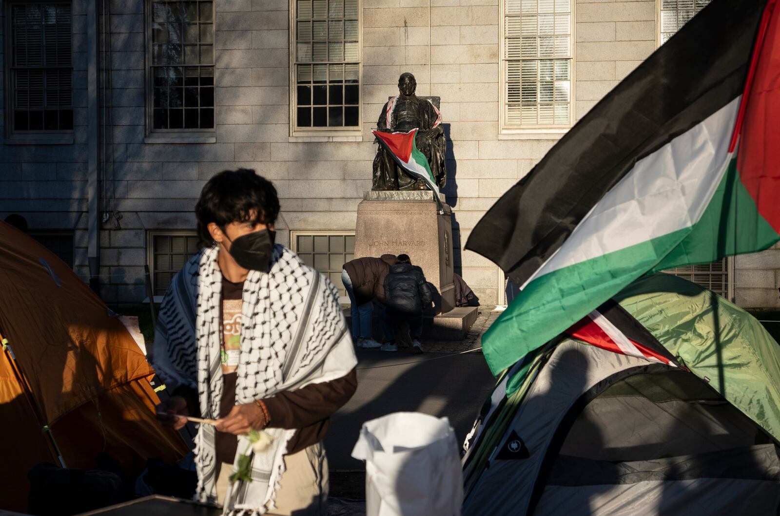 FILE - A student protester stands in front of the statue of John Harvard, the first major benefactor of Harvard College, draped in the Palestinian flag, at an encampment of students protesting against the war in Gaza, at Harvard University in Cambridge, Mass., on April 25, 2024. (AP Photo/Ben Curtis)