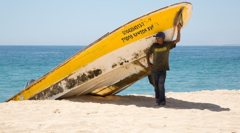 A fisherman stands in the shade under a boat in the small town of Todos Santos, Mexico, July 7, 2016. The town houses the Tres Santos project, which includes plans for more than 1,000 “artisanal homes,” restaurants, a private beach club, and a boutique hotel. Community members and fisherman say the project is the opposite of sustainable building. (Beth Coller/The New York Times)