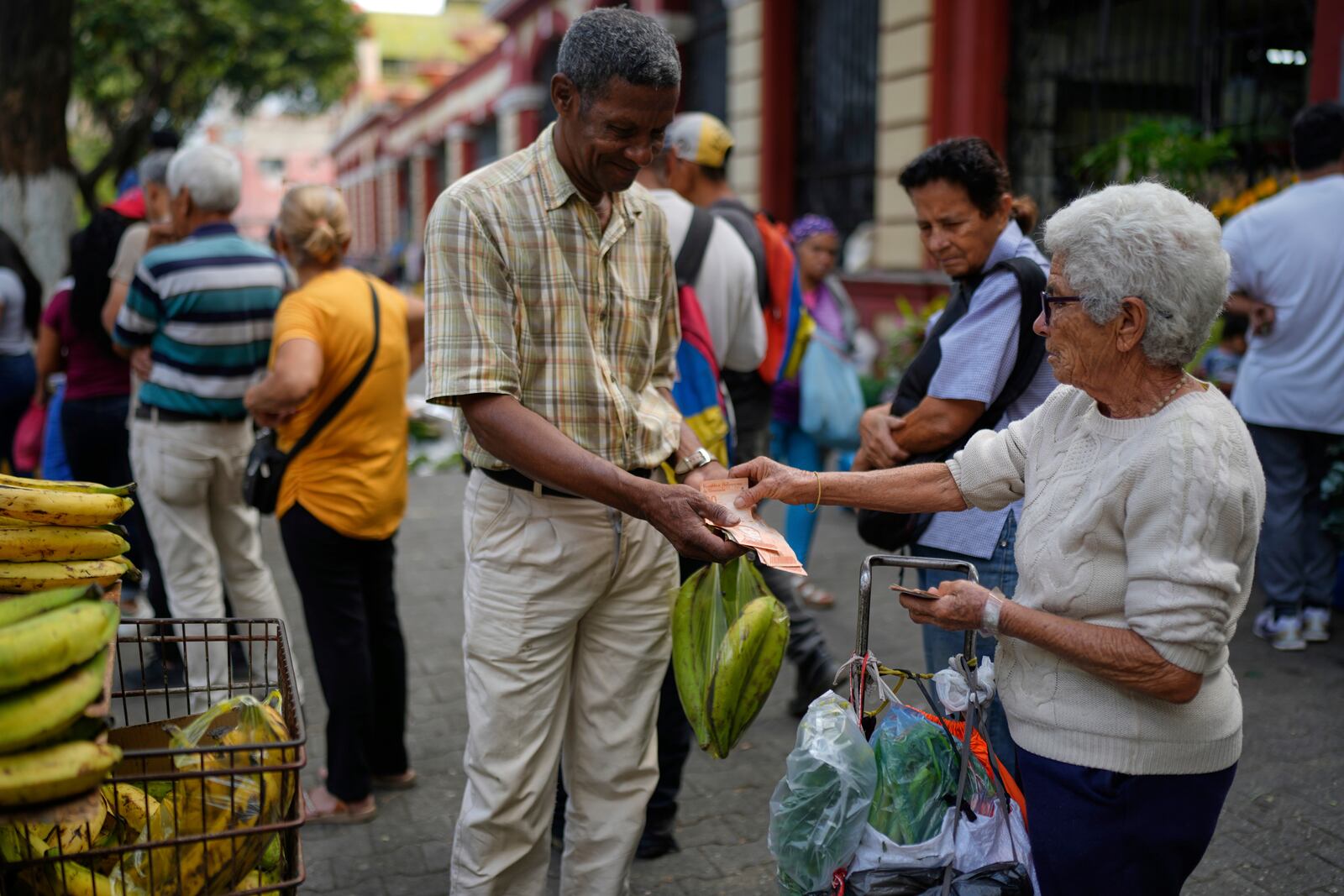 Arnold Guerrero, left, sells plantains to a pedestrian in Caracas, Venezuela, Friday, April 11, 2025. (AP Photo/Ariana Cubillos)