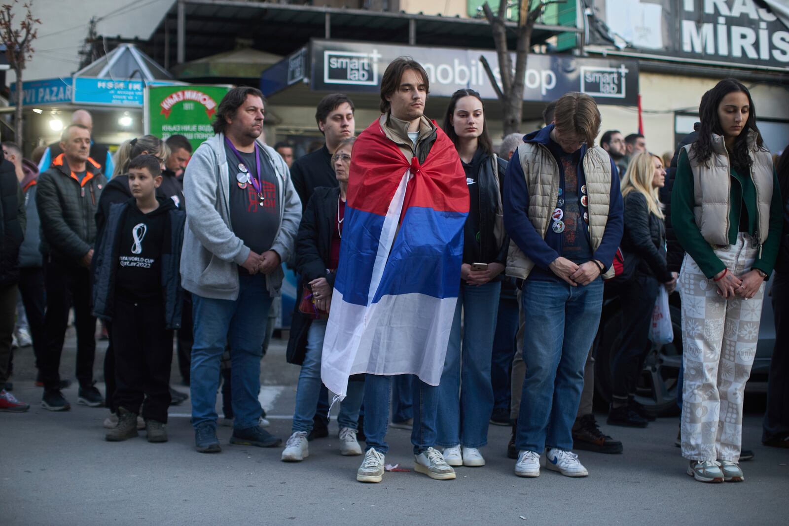 A person draped in the Serbian flag and others observe seventeen minutes of silence during an anti-corruption protest led by university students in the southwestern town of Novi Pazar, Serbia, Saturday, April 12, 2025. (AP Photo/Marko Drobnjakovic)