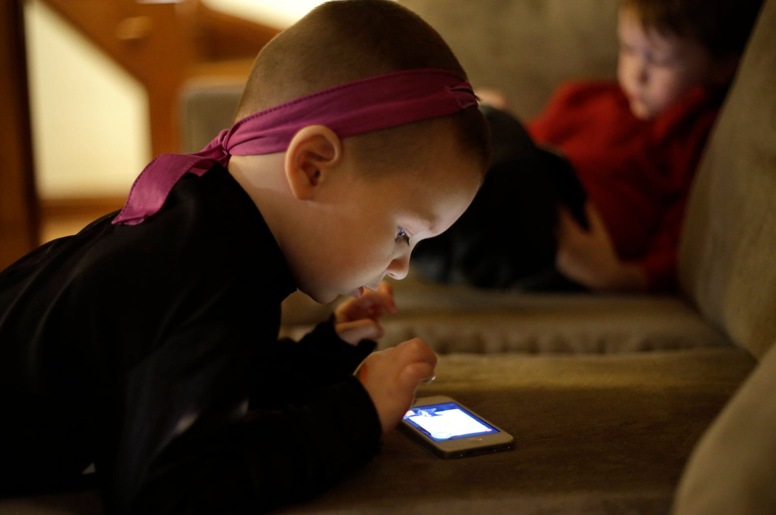 FILE - Nolan Young, 3, front, looks at a smartphone while his brother Jameson, right, 4, looks at a tablet in their home in Boston, Jan. 27, 2014. (AP Photo/Steven Senne, File)