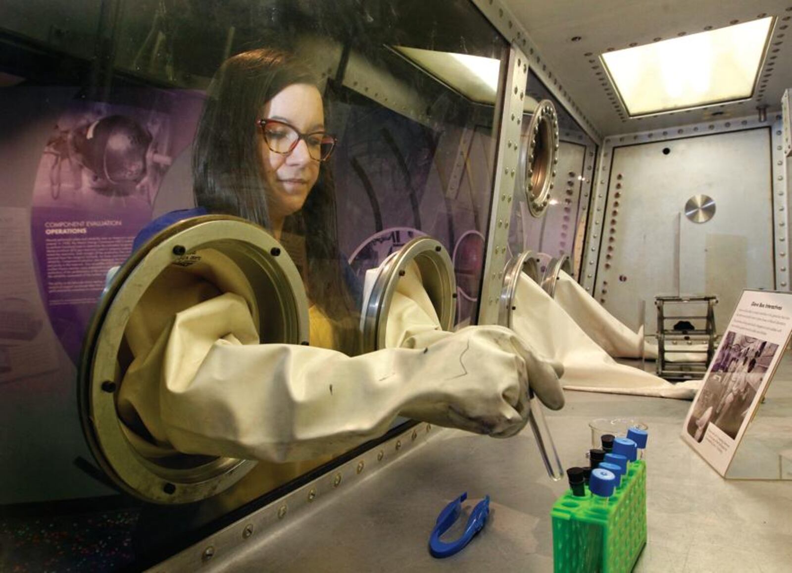 Mandy Askins, the site manager for the Mound Cold War Discovery Center in Miamisburg, demonstrates how Mound Laboratory employees used a glove bos to work with radioactive and dangerous materials. This is one of the interactive activities on site at the new musuem.  LISA POWELL / STAFF