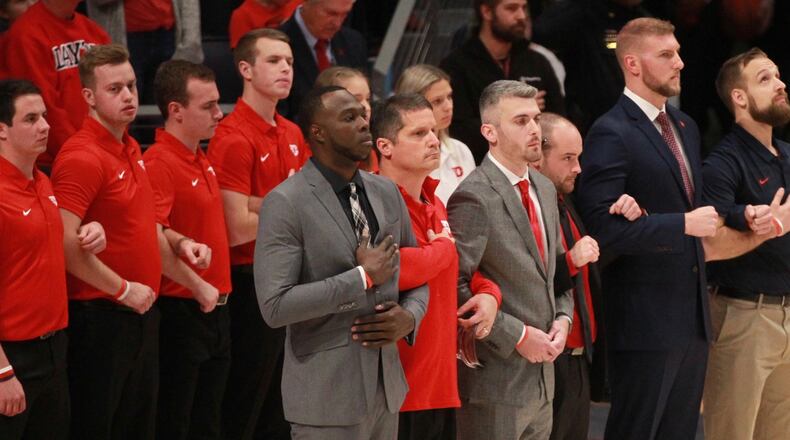Dayton coaches, trainers and managers stand for the national anthem before a game against Indiana State on Nov. 9, 2019, at UD Arena. In the front row, from left to right, are Khyle Marshall, Mike Mulcahey, Brett Comer, James Haring, Sean Damaska and Casey Cathrall. David Jablonski/Staff