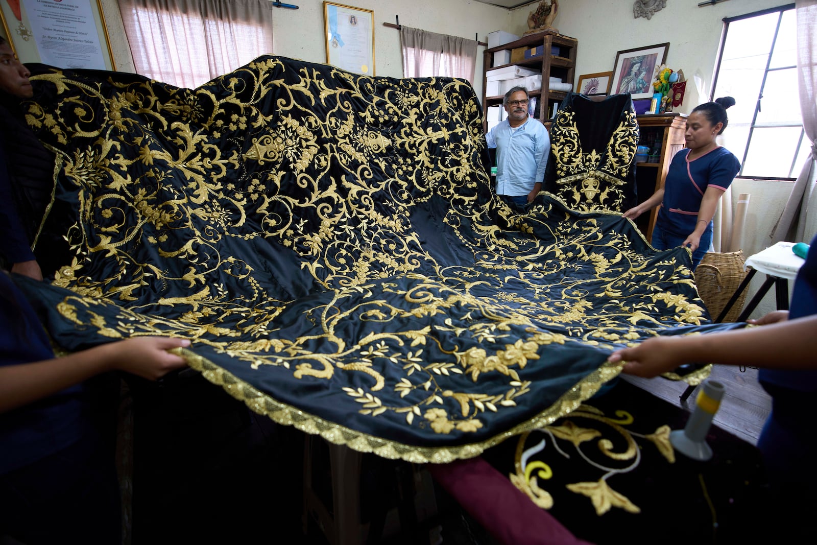 Guatemalan artist Alejandro Juarez, top center, and weavers display their finished tunic to be worn by a statue of the Virgin Mary, at the Maria Auxiliadora embroidery workshop in San Miguel Escobar, Guatemala, Wednesday, April 2, 2025. (AP Photo/Moises Castillo)