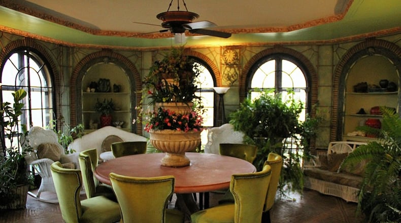 An octagonal conservatory features leaded glass French doors framed by brick-trimmed arches, iron trellises, herringbone brick flooring, molded plaster trim with floral motifs and abundant natural light to nurture various plants.
