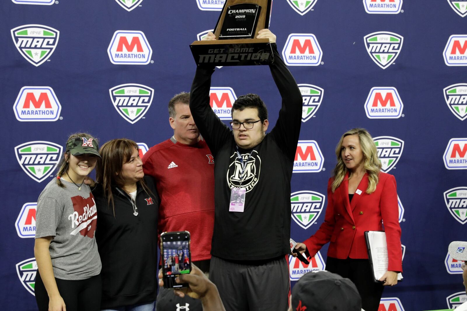 Max Martin, the son of Miami football coach Chuck Martin, holds up the MAC Championship trophy on Dec. 7, 2019, at Ford Field in Detroit. Chuck is behind him. From fart left is Chuck s daughter, Emma, and his wife Dulcie. CONTRIBUTED