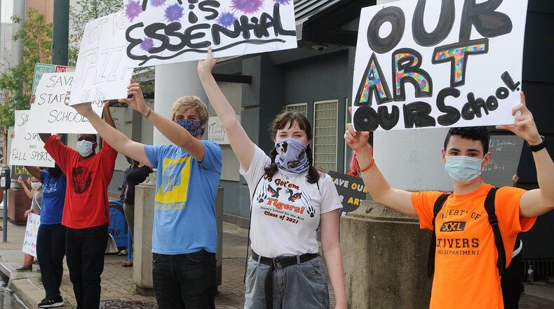 A crowd of people protest layoffs of teachers, especially in the arts, outside the Dayton Public Schools headquarters building on Ludlow Street Aug. 28, 2020.