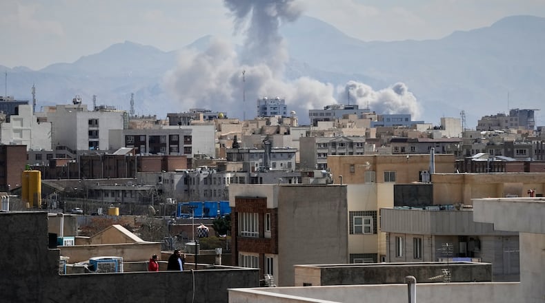 People watch from a rooftop as a plume of smoke rises after a strike in Tehran, Iran, Sunday, March 1, 2026. (AP Photo/Vahid Salemi)