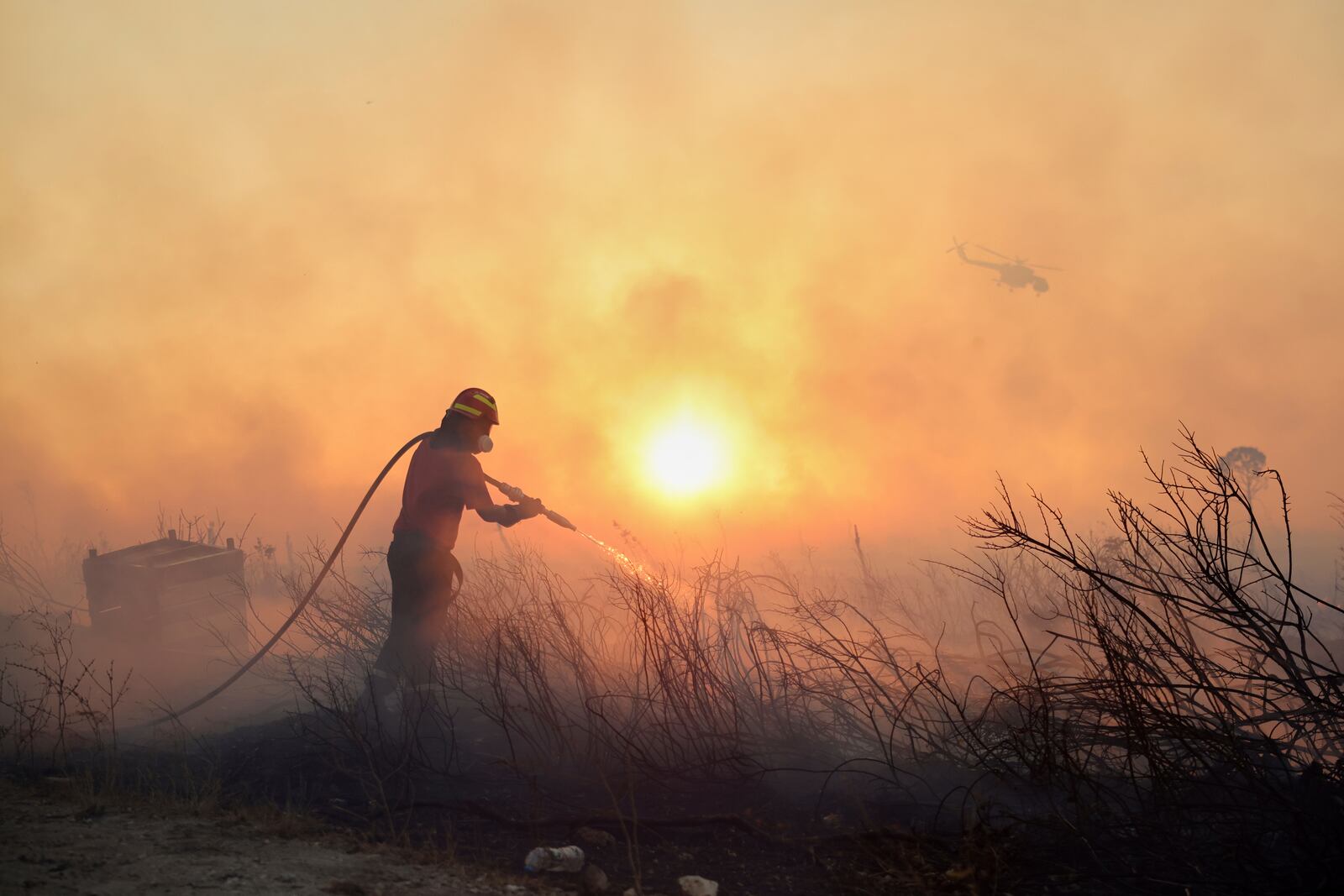 A firefighter tries to extinguish a wildfire as a helicopter flies, in the northwestern suburb of Kryoneri, in Athens, Greece, Saturday, July 26, 2025. (AP Photo/Yorgos Karahalis)