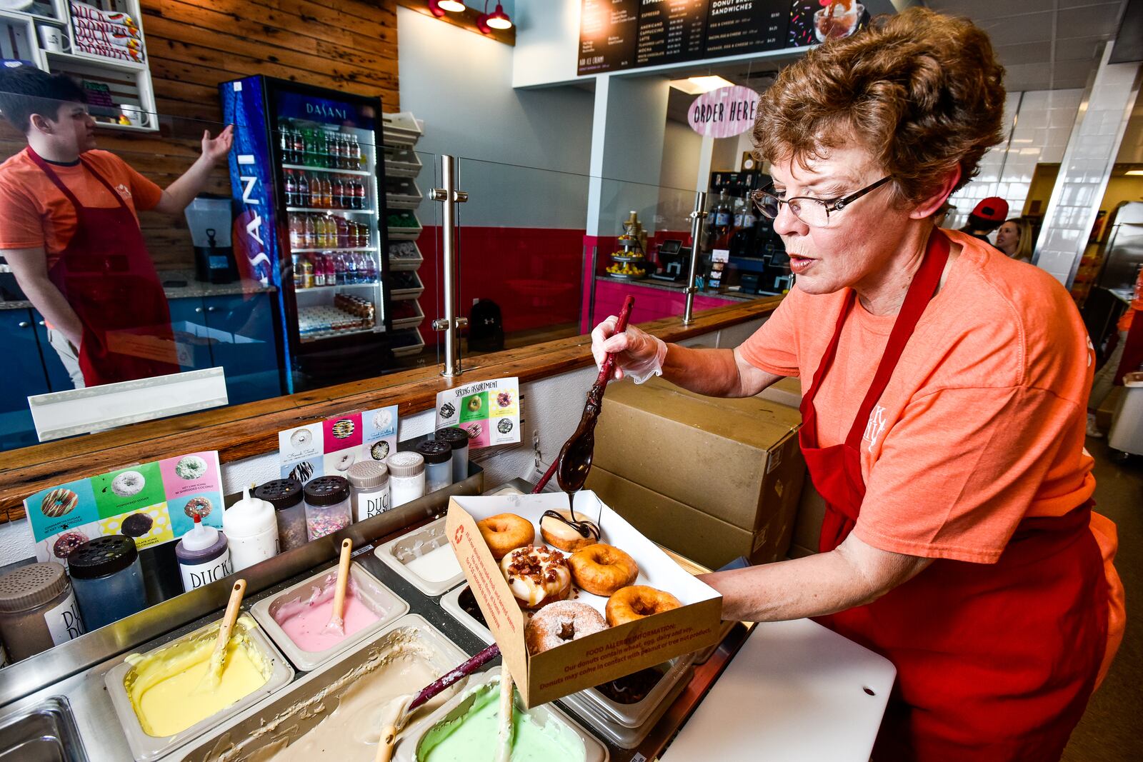 Connie Cordes prepares donuts at Duck Donuts as they opened their doors for a preview event Thursday, April 12. Duck Donuts opens April 13 in Deerfield Towne Center in Mason. The donut shop offers fresh made-to-order donuts with a variety of toppings. NICK GRAHAM/STAFF
