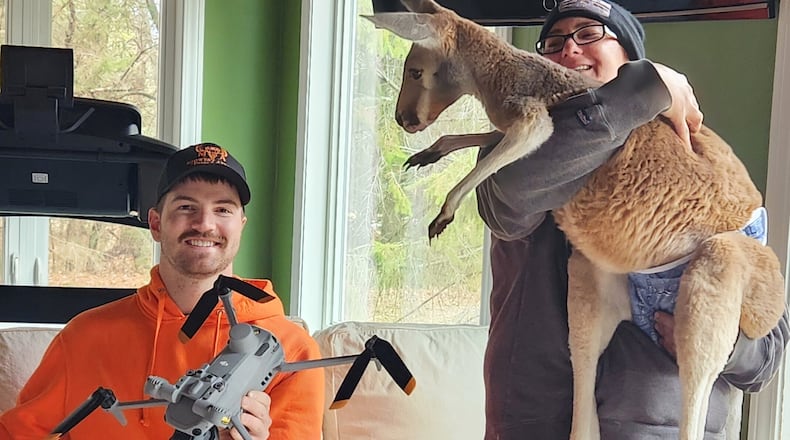 This photo provided by Cara Johnson shows her husband and drone operator, Colton Johnson, left, sitting next to Stacy Brereton as she holds a kangaroo named Chesney at Sunshine Farm, in Necedah, Wis., Saturday, March 28, 2026. (Cara Johnson via AP)