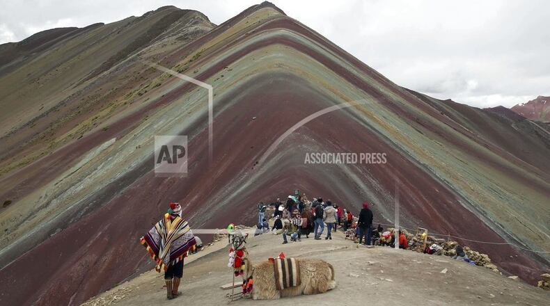 In this March 2, 2018 photo, an Andean man rests with his llama on Rainbow Mountain in Pitumarca, Peru. Tourists gasp for breath as they climb for two hours to the 16,404-foot (5,000-meter) peak in the Peruvian Andes, but stunned by the magical beauty that unfurls before them. (AP Photo/Martin Mejia)