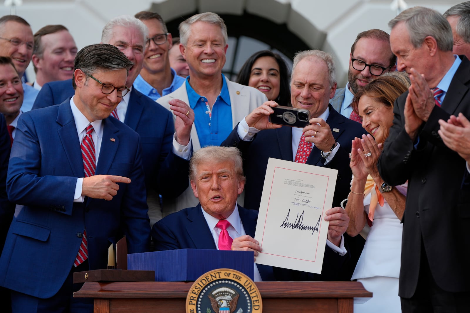 President Donald Trump holds his signed his signature bill of tax breaks and spending cuts at the White House, Friday, July 4, 2025, in Washington, surrounded by members of Congress. (AP Photo/Julia Demaree Nikhinson)