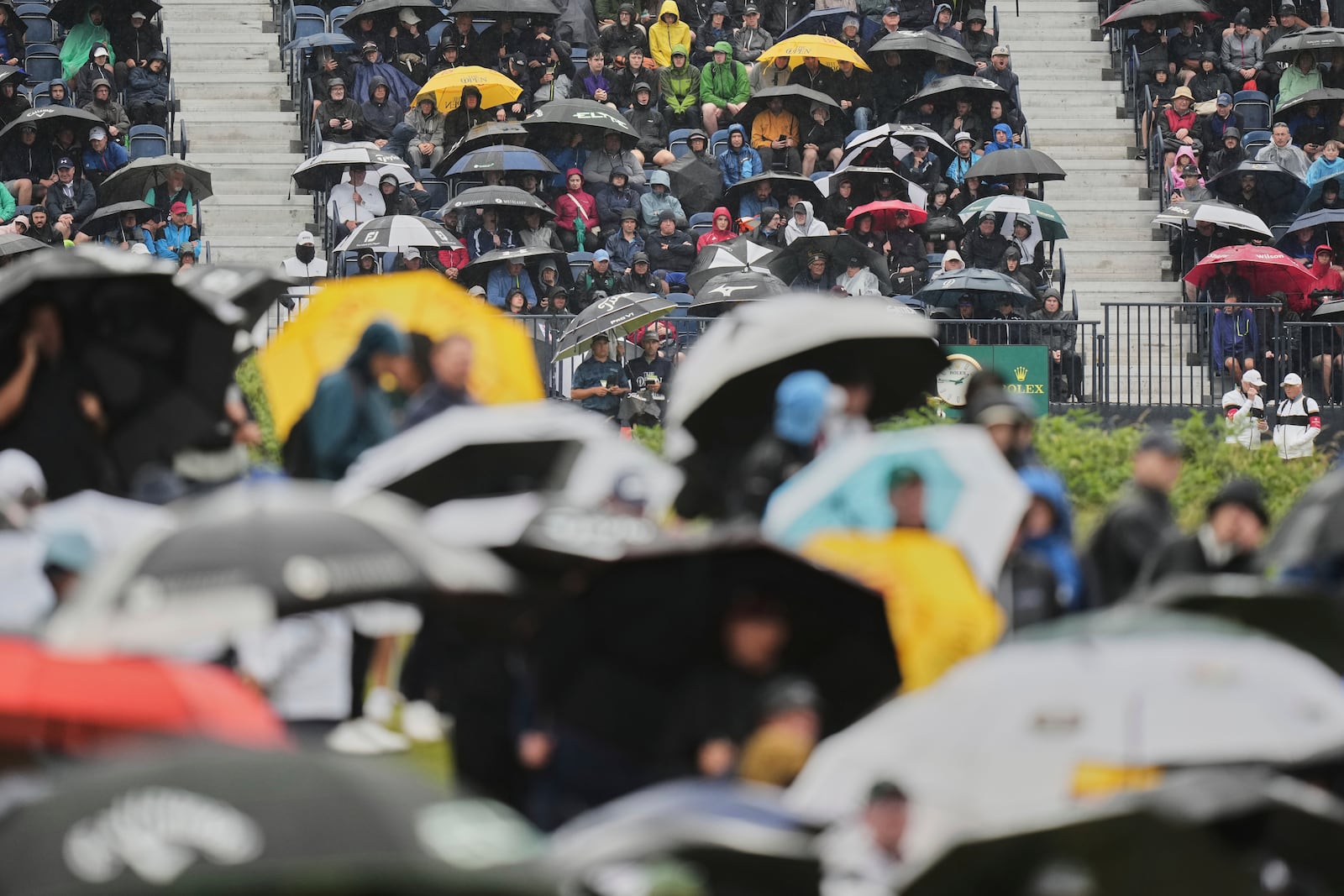 Spectators hold up umbrellas as heat rain falls during the first round of the British Open golf championship at the Royal Portrush Golf Club, Northern Ireland, Thursday, July 17, 2025. (AP Photo/Francisco Seco)