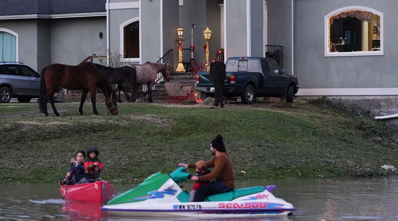 "E-man" Trujillo uses a jet-ski to pull his children in a canoe as the family's horses graze on high ground in near their front door after heavy rains led to historic flooding in the region Saturday, Dec. 13, 2025, in Burlington, Wash. (AP Photo/Lindsey Wasson)
