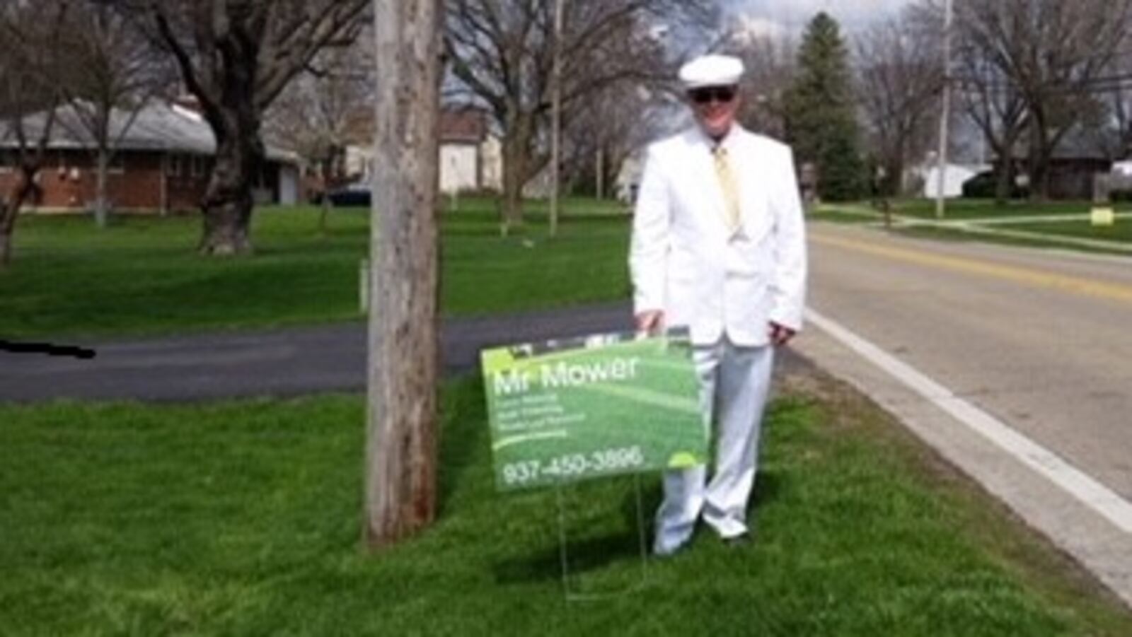 Joshua Vanderpool stands behind a sign for his lawn mowing business