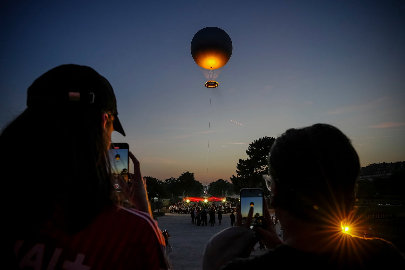 People take pictures as the helium ballon that was used during the 2024 Olympic Games as the Olympic cauldron is launched in the Tuileries Gardens of Paris on Saturday, June 21, 2025. (AP Photo/Aurelien Morissard)