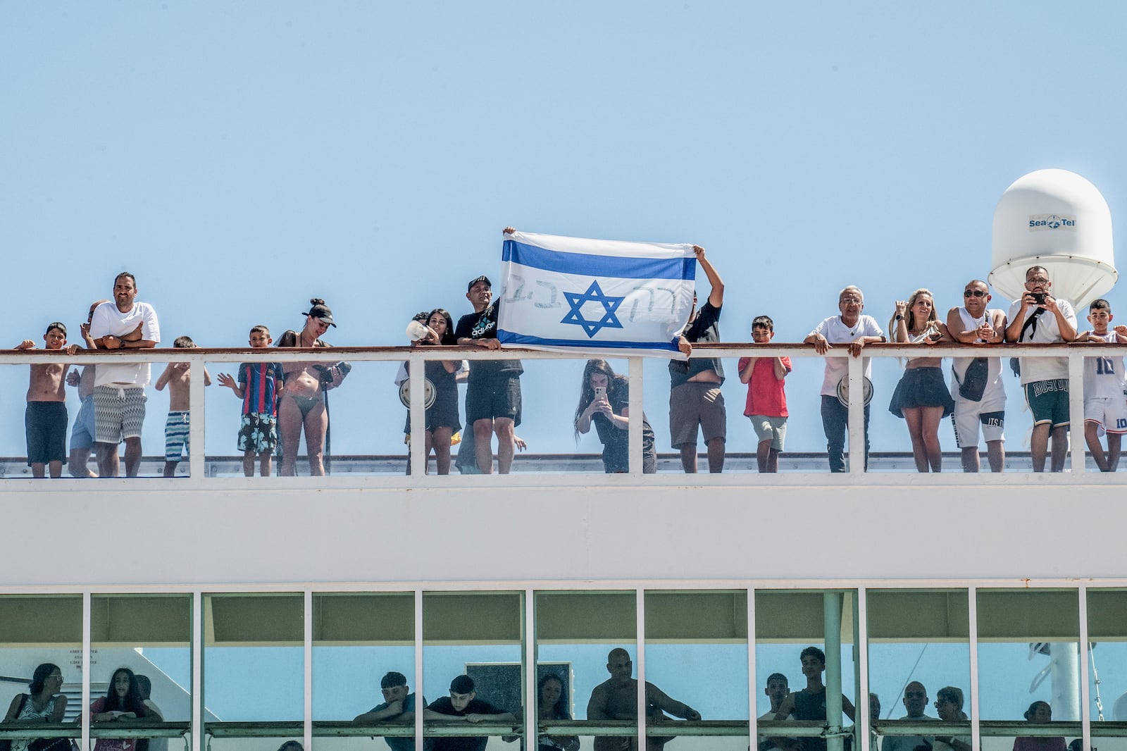 Israeli tourists hold the flag of their country as a cruise ship arrives at Agios Nikolaos port, on the island of Crete, Greece, Tuesday, July 29, 2025. (Antonis Zouridakis/Eurokinissi via AP)