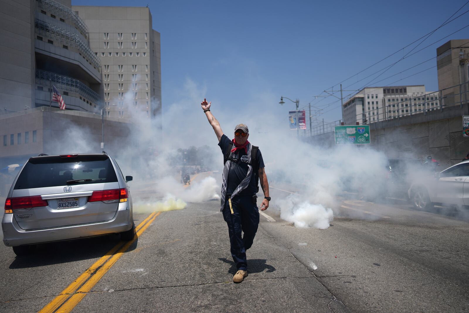 A protester displays a poster as tear gas is used in the metropolitan detention center of downtown Los Angeles, Sunday, June 8, 2025, following last night's immigration raid protest. (AP Photo/Eric Thayer)