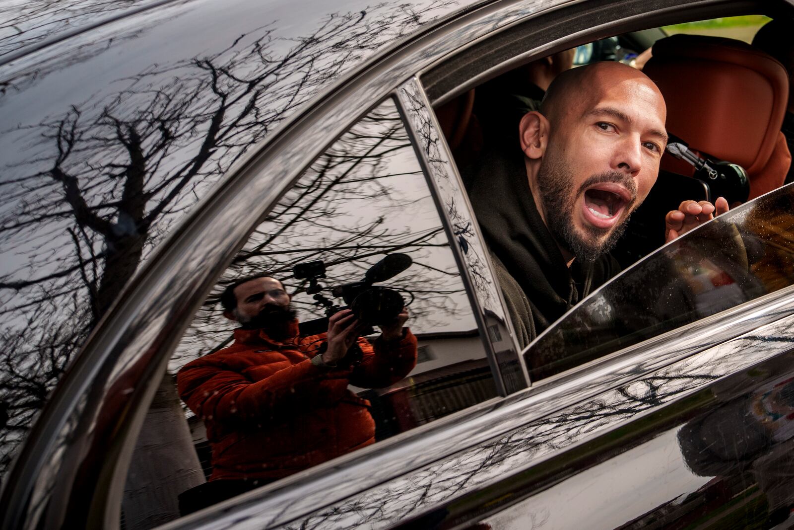 Andrew Tate speaks to media as he leaves in a vehicle after checking in at a police station as part of his judicial control, which requires him to appear before judicial authorities in Romania when summoned, in Voluntari, Romania, Monday, March 24, 2025. (AP Photo/Vadim Ghirda)