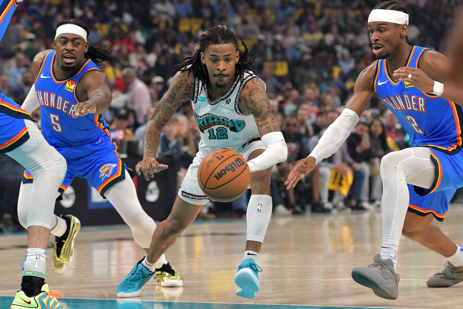 Memphis Grizzlies guard Ja Morant (12) handles the ball between Oklahoma City Thunder guards Shai Gilgeous-Alexander (2) and Luguentz Dort (5) in the first half of Game 3 of an NBA first-round playoff series Thursday, April 24, 2025, in Memphis, Tenn. (AP Photo/Brandon Dill)