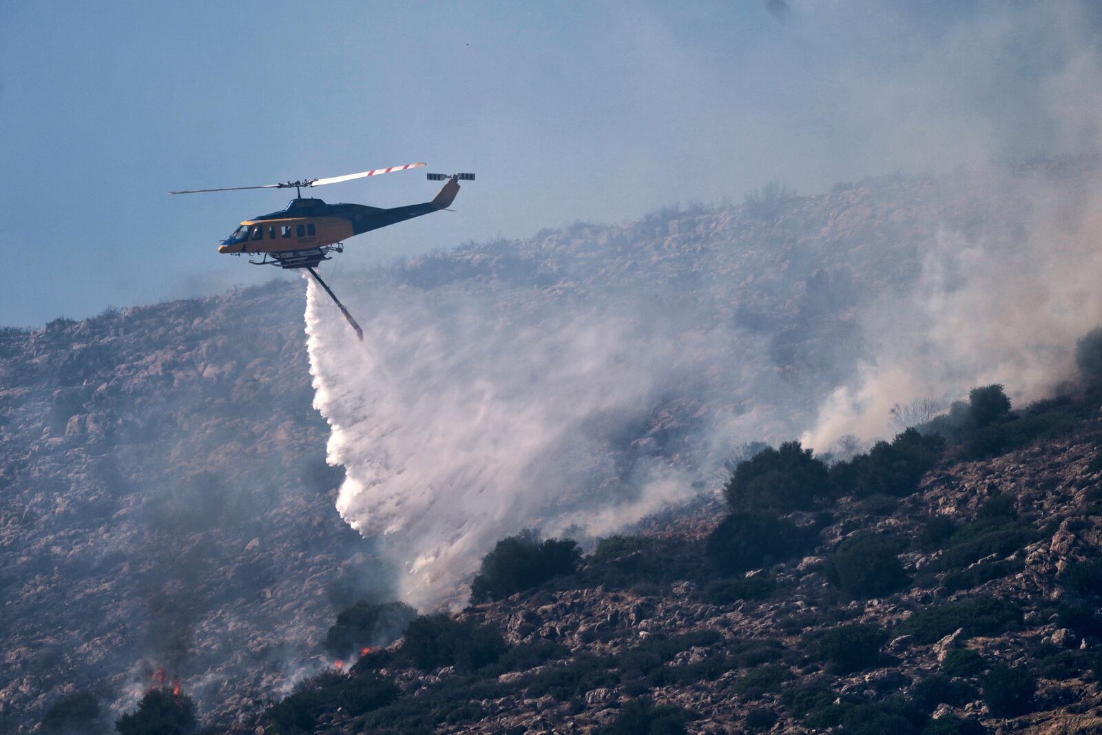 A firefighting helicopter drops water while battling a blaze in the seaside area of Palaia Fokaia, south of Athens, Thursday, June 26, 2025, as authorities evacuate five locations during Greece's first summer heatwave with temperatures nearing 40 degrees Celsius (104 Fahrenheit). (AP Photo/Thanassis Stavrakis)