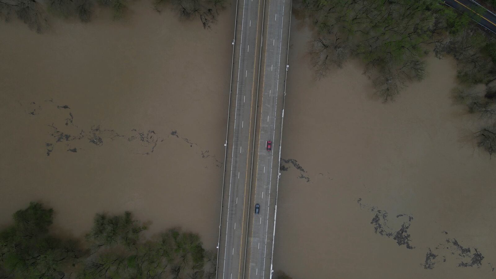 An aerial view of debris floating down the Kentucky River as vehicles drive over a bridge Saturday, April 5, 2025, in Frankfort, Ky. (AP Photo/Jon Cherry)