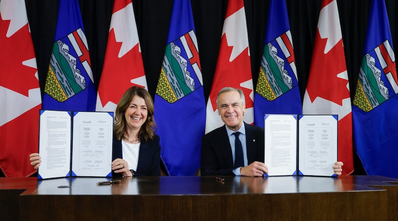 Prime Minister Mark Carney, right, signs an MOU with Alberta Premier Danielle Smith in Calgary, Alta., Thursday, Nov. 27, 2025. (Jeff McIntosh /The Canadian Press via AP)