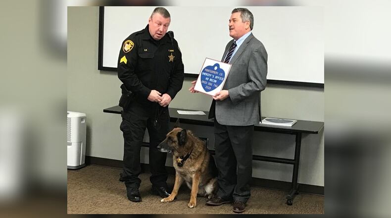 Montgomery County Auditor Karl Keith, right, presents a 2019 dog license to K-9 Recon and his handler, deputy Troy Bodine.
