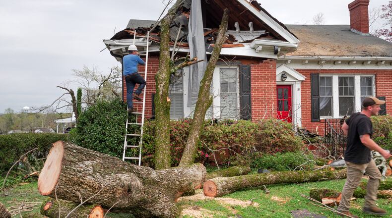 People work to clear a tree from a storm damaged home in Newnan, Ga., on Friday, March 26, 2021. Dozens of tornadoes tore across Alabama and Georgia beginning on Thursday, leaving at least six dead and many neighborhoods in tatters. (Johnathon Kelso/The New York Times)