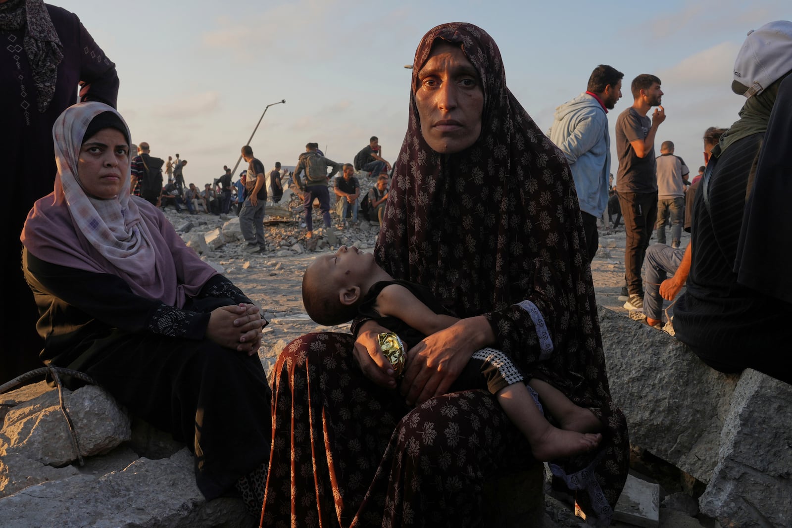 Somoud Wahdan looks at the camera as she sits with her child in an area in the northern Gaza Strip, while waiting for trucks with humanitarian aid to arrive, in Gaza City, Friday, July 25, 2025. (AP Photo/Abdel Kareem Hana)