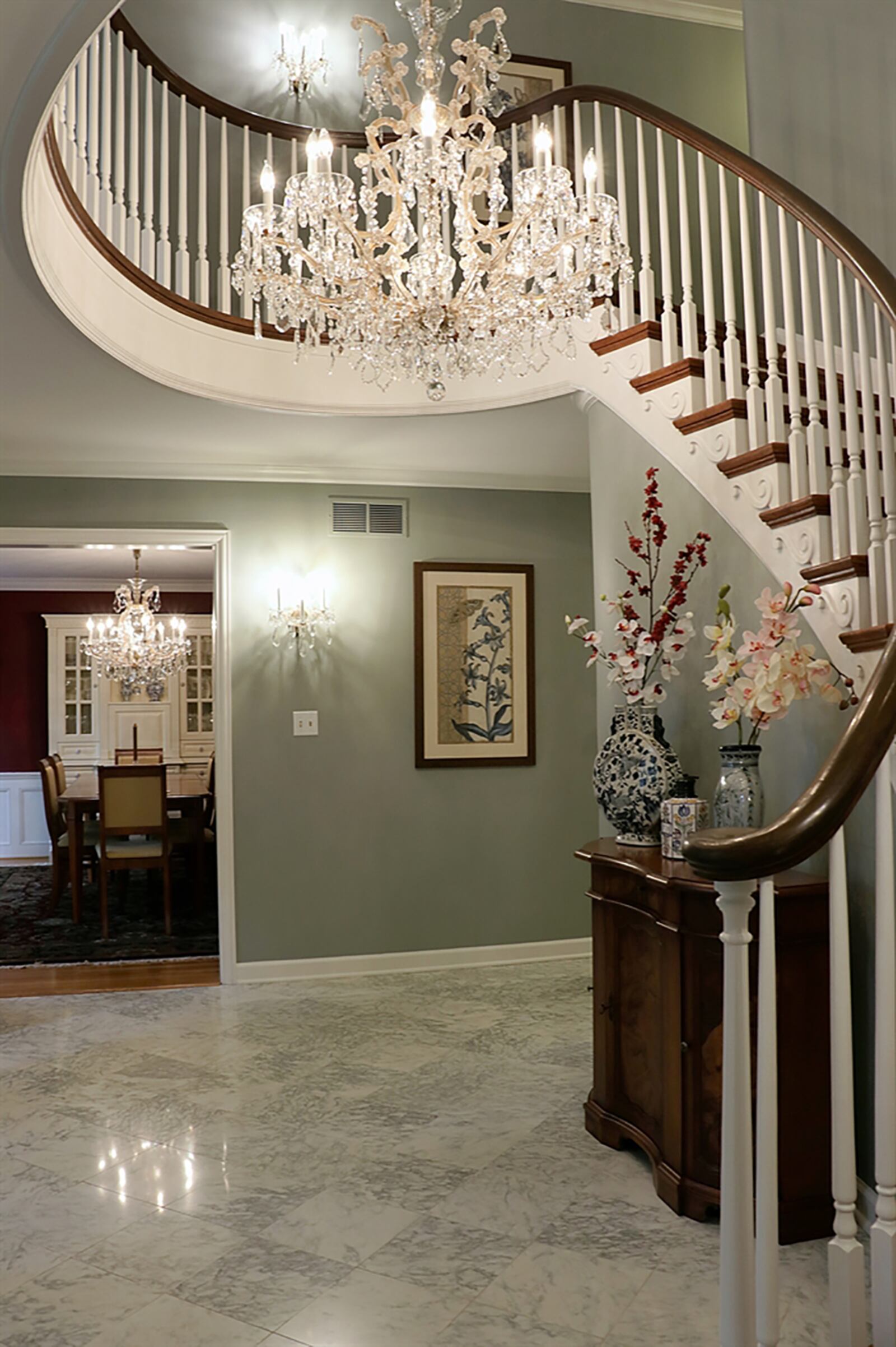 The home’s formal entry has a marble floor. A curved staircase with detailed railing wraps up a curved wall and around a crystal chandelier to the second-floor loft with window nook. CONTRIBUTED PHOTO BY KATHY TYLER