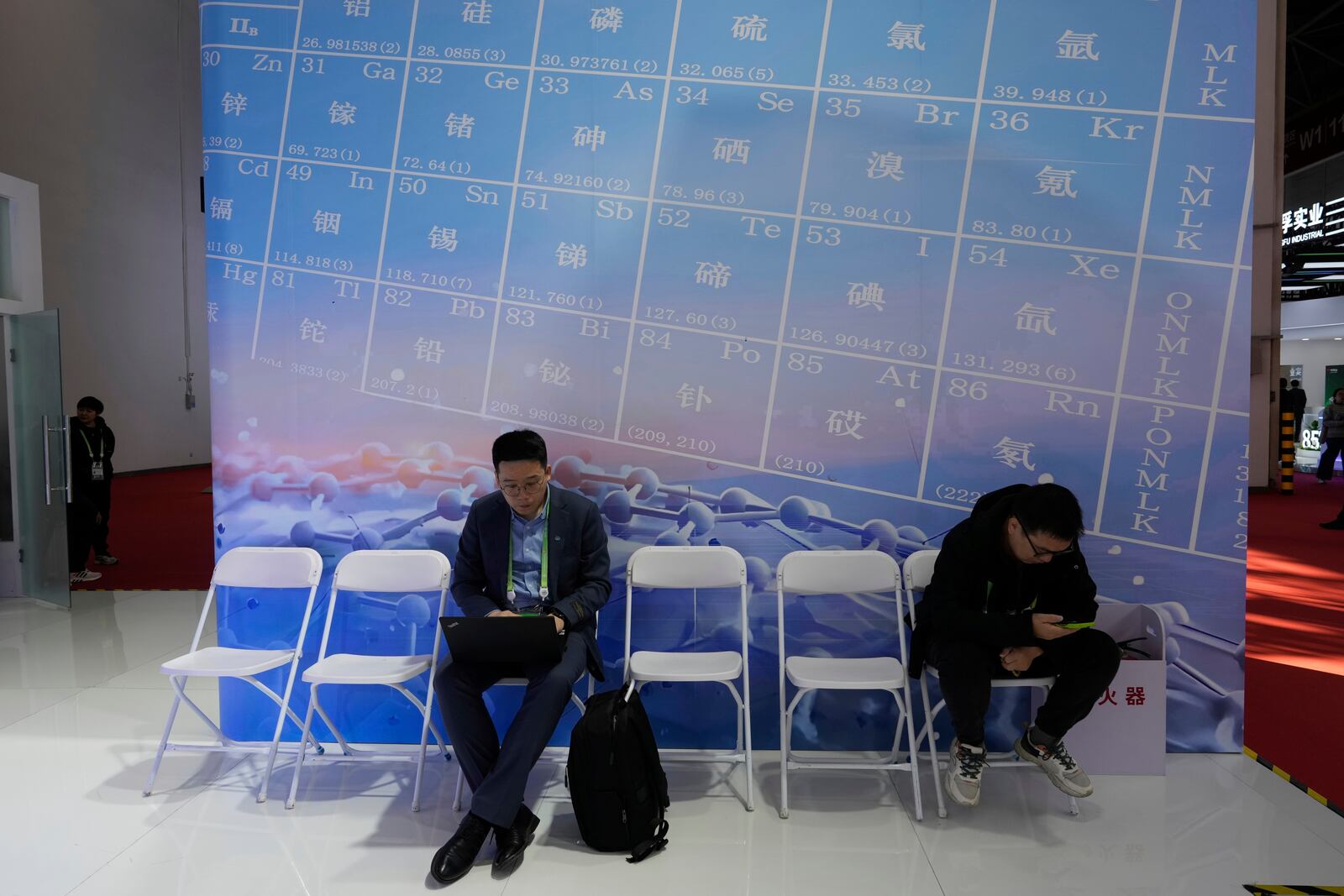 Men sit near a periodic table showing minerals at the China International Supply Chain Expo in Beijing, on Nov. 27, 2024. (AP Photo/Ng Han Guan)