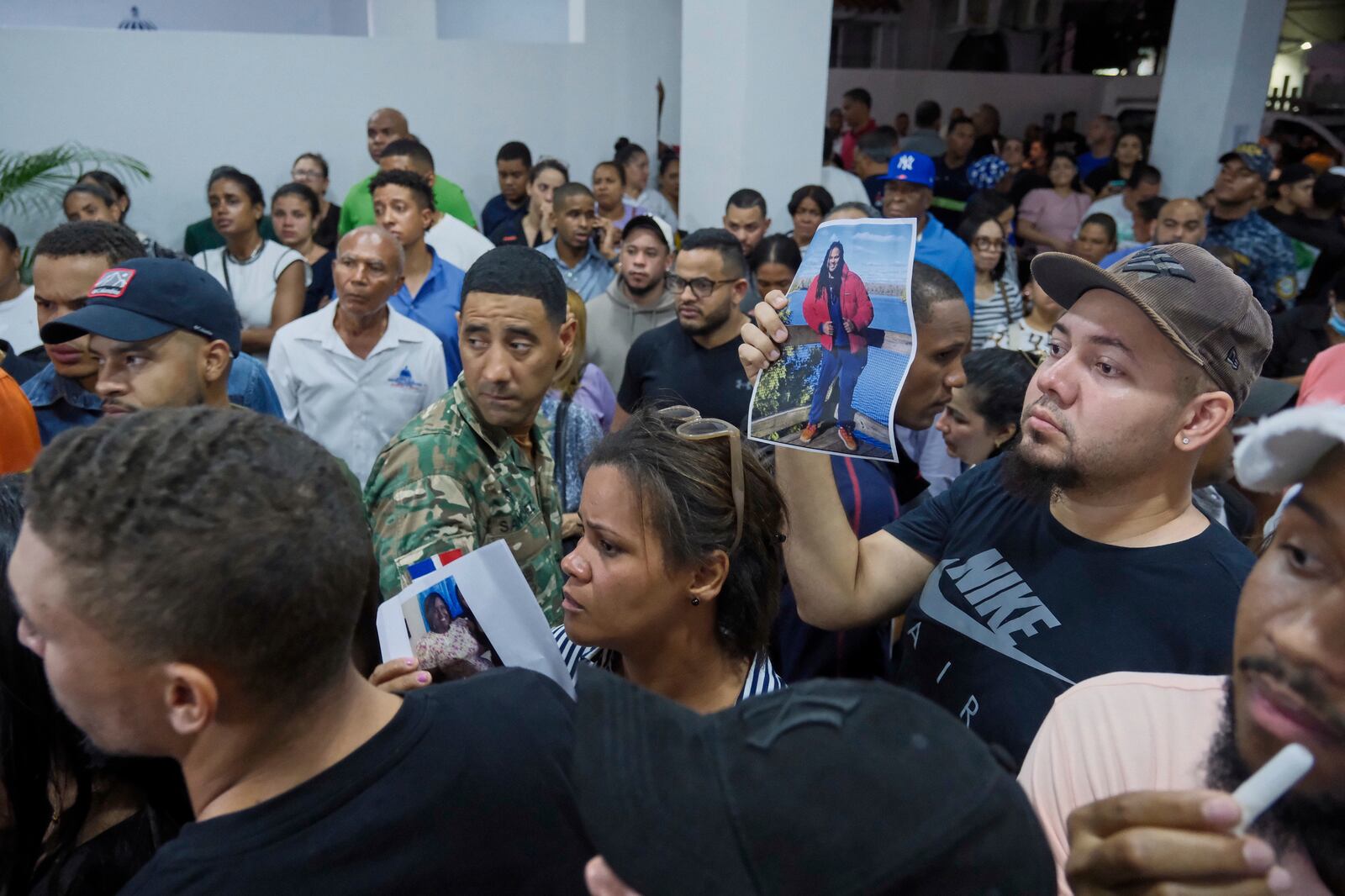 People hold up photos of their relatives while waiting to identify them at the National Institute of Forensic Pathology after the roof collapsed at Jet Set nightclub during a merengue concert in Santo Domingo, Dominican Republic, Tuesday, April 8, 2025. (AP Photo/Ricardo Hernandez)