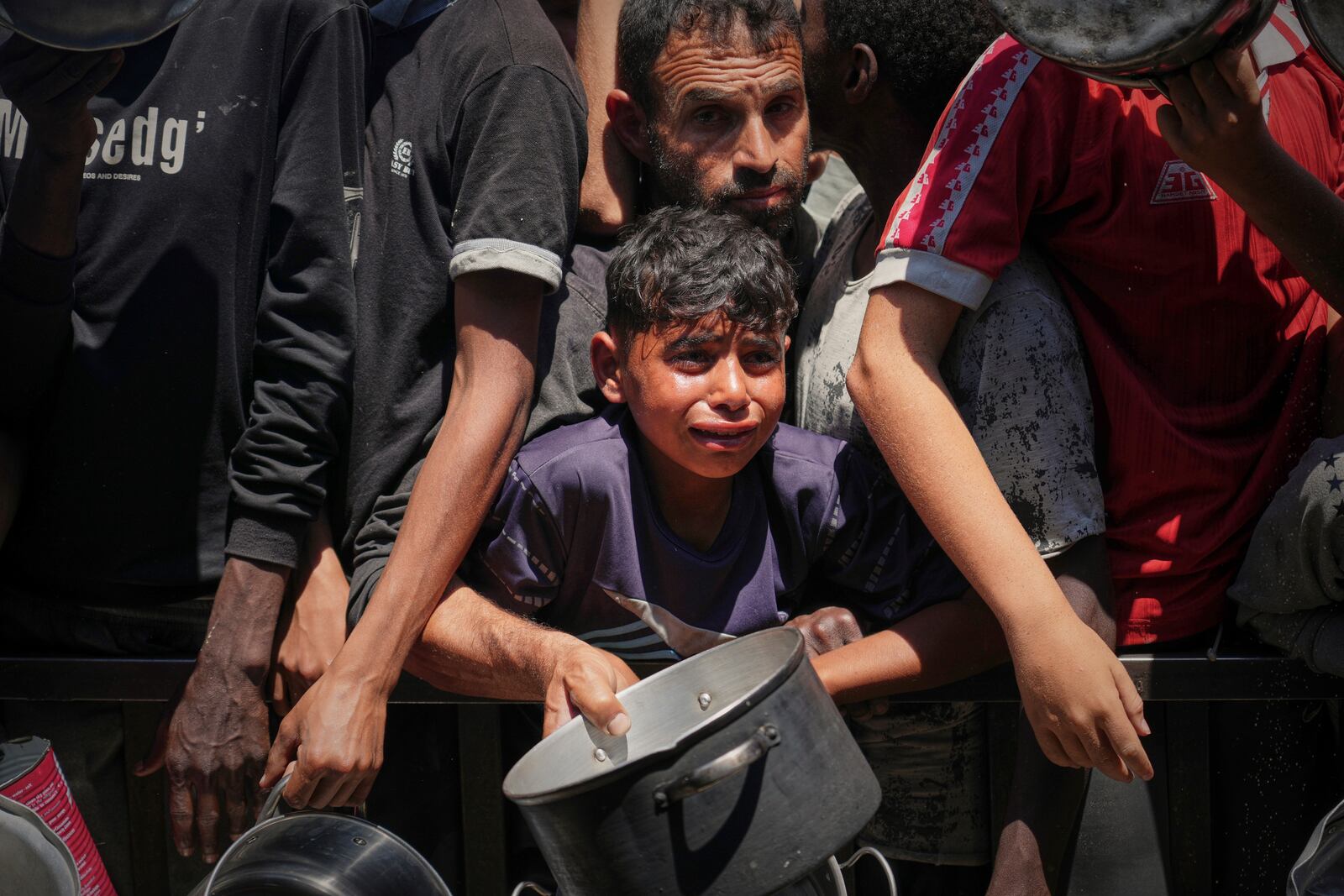 Palestinians struggle to receive cooked food distributed at a community kitchen in the Muwasi area of Khan Younis, in the Gaza Strip, Friday, May 23, 2025. (AP Photo/Abdel Kareem Hana)