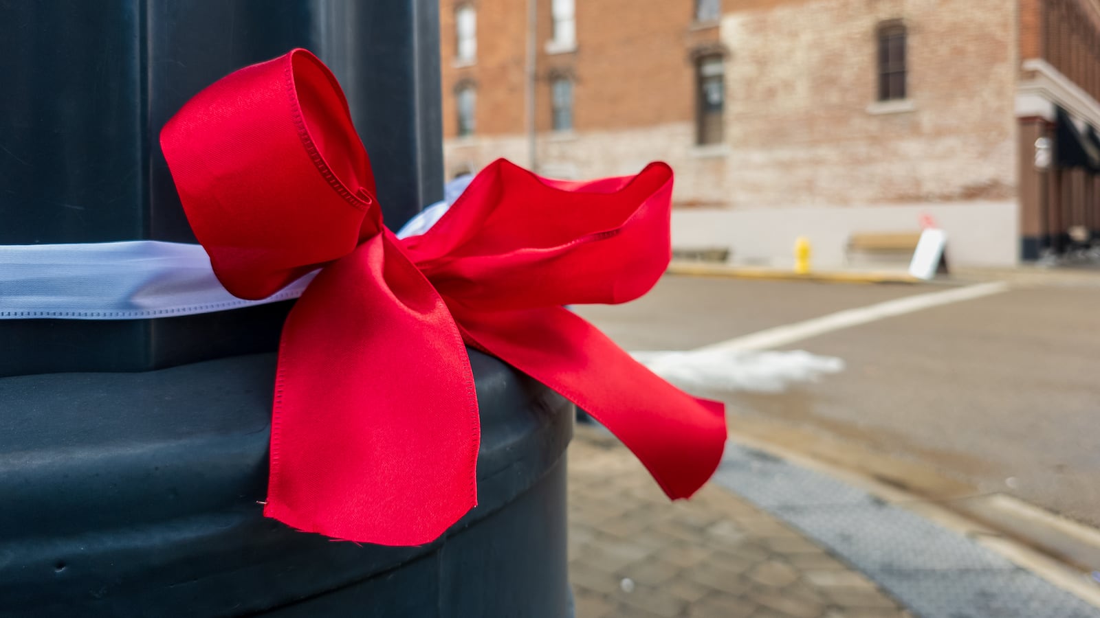 Red and white ribbons tied with bows have been attached to traffic poles, lampposts and trees along Main Street in Tipp City’s downtown historic district in memory of Ashley Flynn, a 37-year-old mother of two who was fatally shot during a reported home burglary early on Monday, Feb. 16. Area residents said on Wednesday the crime has shocked the close-knit community. BRYANT BILLING / STAFF